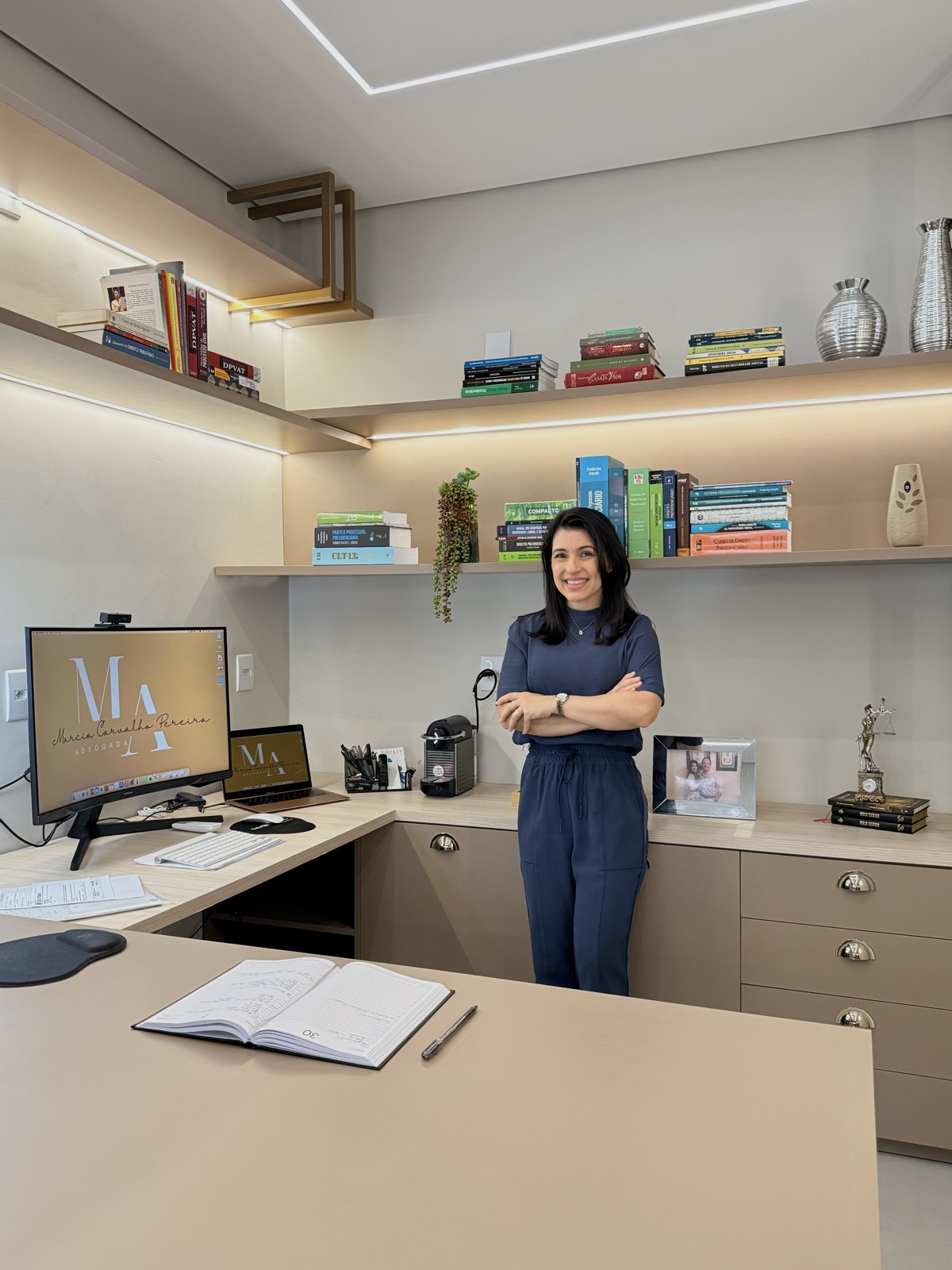 Dra. Marcia Carvalho Pereira em sua mesa de trabalho, com livros de Direito Previdenciário ao fundo